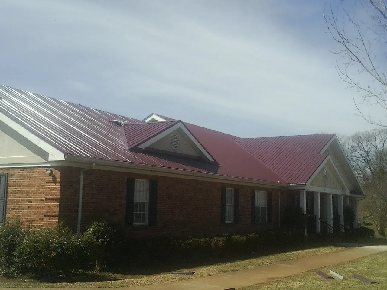 Red metal roof with gabled entries on a long brick building, from a Hail Damage Roof Repair job in Whitesburg