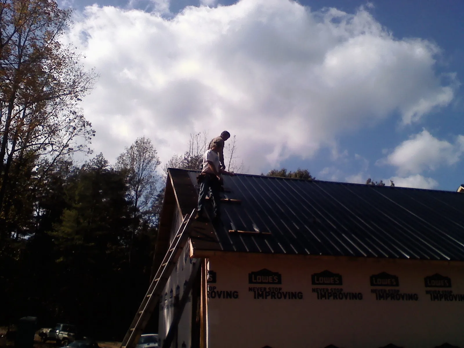Roofer fastening dark metal panels high against a cloudy sky, from a Roof Inspection job in Whitesburg